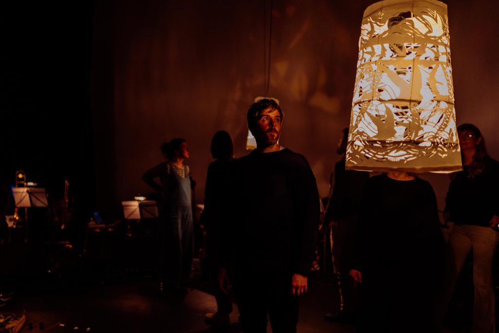 Photograph of Jack in a low lit music room looking towards a lampshade cut our with bird shapes.